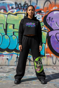 JuneBug Women's Wide-Leg Sweatpants in black with graffiti logo down the leg, worn by a woman in a relaxed streetwear outfit